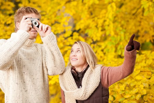 Young happy couple making photo in autumn park pointing at