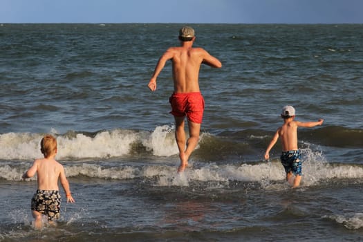 Father and his two sons running into the ocean and having fun