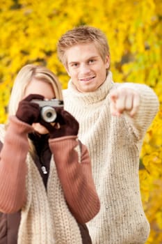 Young happy couple woman making photo in autumn park pointing