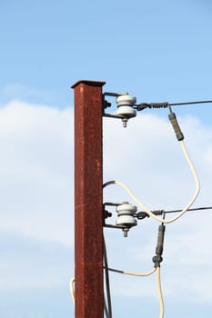 A rusty old power pole with a cloudy, blue sky.