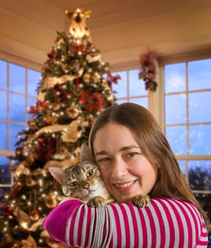 Young bengal kitten held on arm of young woman in front of brightly lit christmas tree