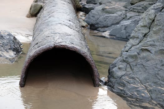 a rusty overflow pipe coming from the land to the sea