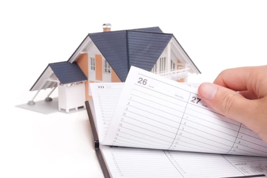 Moving house planning concept. Model of house and man browse through personal organizer.