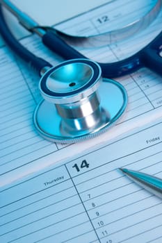 Planning routine medical exam represented by part of stethoscope, calendar and pen. Family doctor workplace.