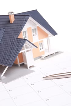 Moving house planning concept. Model of house situated on calendar. Focused on pen.