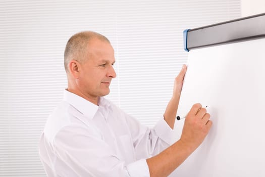 Handsome mature businessman writing at empty flip chart looking aside