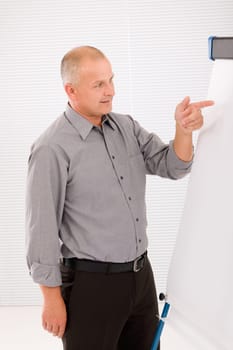 Mature handsome businessman pointing at empty flip chart looking aside