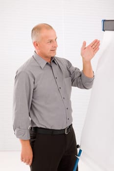 Mature handsome businessman pointing at empty flip chart looking aside