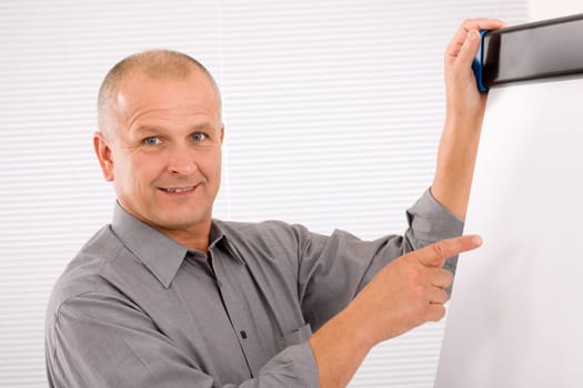 Mature handsome businessman pointing at empty flip chart looking aside