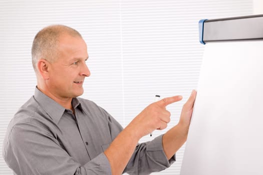Handsome mature businessman writing at empty flip chart looking aside