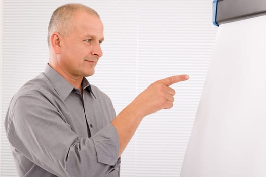 Mature handsome businessman pointing at empty flip chart looking aside