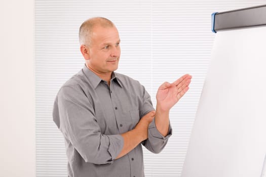 Mature handsome businessman pointing at empty flip chart looking aside