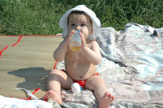 baby with a hat and bottle in the beach