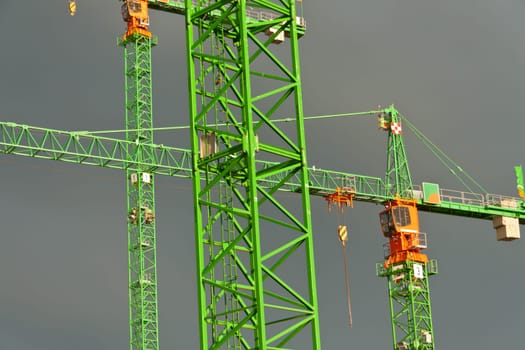 Construction cranes struck by the sun in front of dark clouds