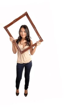 A lovely Asian woman in jeans and a beige blouse holding up a picture frame for her head, standing in the studio for white background.