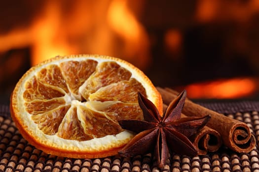 Orange slice,anime nuts and cinnamon sticks in front of a fireplace