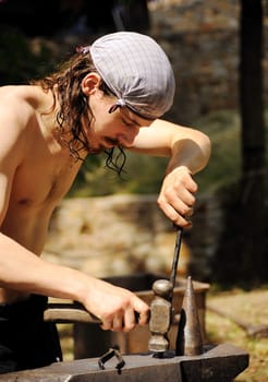 Young blacksmith hammering hot iron on anvil