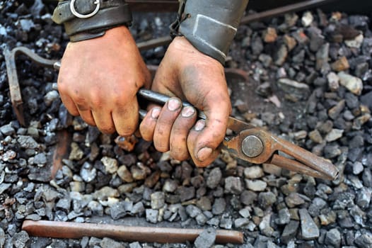 Detail of dirty hands holding pliers - blacksmith