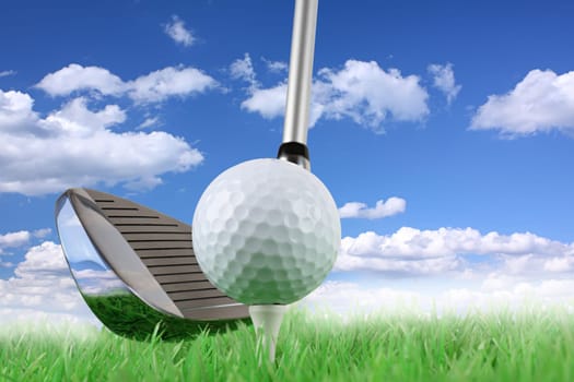 Golf club with ball on tee on meadow in front of blue sky.