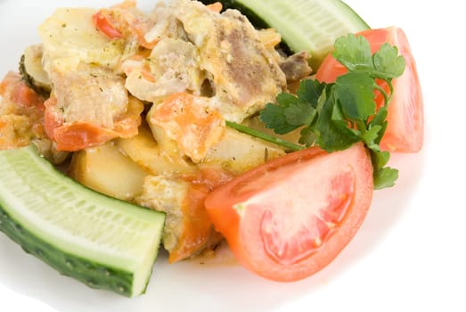 Close up of meat, potatoes, tomatoes and cucumbers dish on white