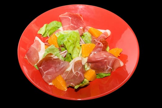 jamon with orange fruit and lettuce at red dish on black