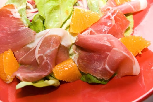 Close up of Salad: jamon with orange fruit and lettuce at red dish on white. It is very delicious food