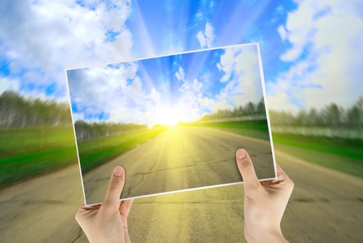 Hand holding photo of road background with sunrise