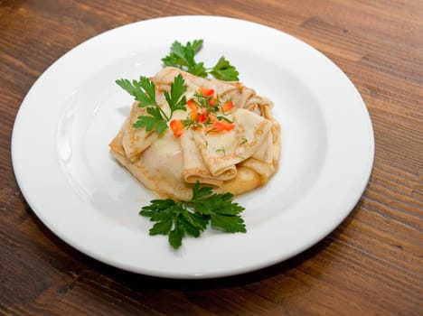 Pancakes with greenery on white plate at wood table