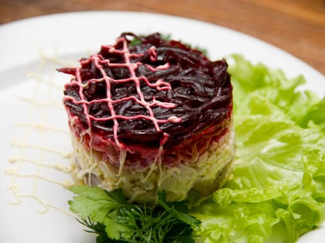 Tasty fresh healthy salad with herring on wooden table background. Russian dish.