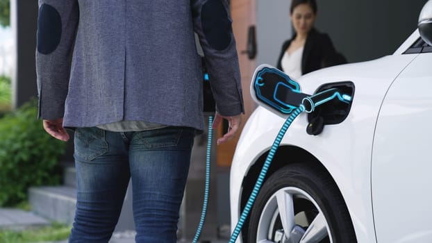 Modern family couple recharge electric car, EV charger from home charging station plugged in EV car in house garage. Smart and futuristic home energy infrastructure. Peruse