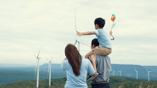 Concept of progressive happy family enjoying their time at the wind turbine farm. Electric generator from wind by wind turbine generator on the country side with hill and mountain on the horizon.