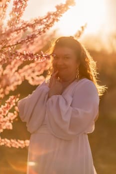 Woman blooming peach orchard. Against the backdrop of a picturesque peach orchard, a woman in a long white dress enjoys a peaceful walk in the park, surrounded by the beauty of nature