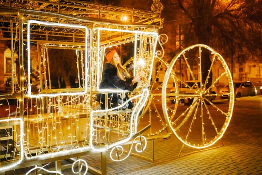 Woman holding sparkler night while celebrating Christmas outside. Dressed in a fur coat and a red headband. Blurred christmas decorations in the background. Selective focus.