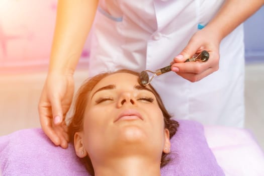 Relaxing massage. Side view european woman getting massage with jade face roller gouache in spa salon.