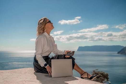 Freelance women sea working on a computer. Pretty middle aged woman with computer and phone outdoors with beautiful sea view. The concept of remote work