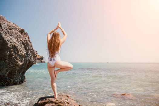 Woman sea yoga. Back view of free calm happy satisfied woman with long hair standing on top rock with yoga position against of sky by the sea. Healthy lifestyle outdoors in nature, fitness concept