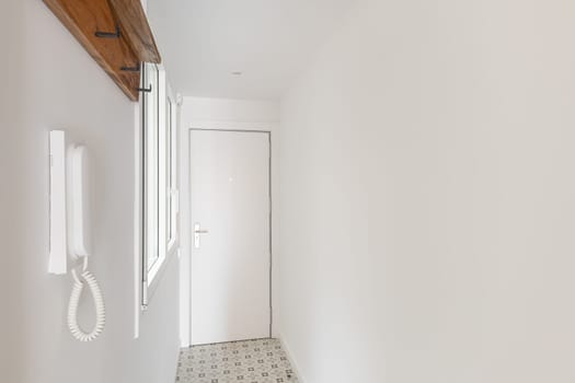 Empty apartment lobby with window, coat rack and intercom. Renovated long hallway with white walls in contemporary house interior