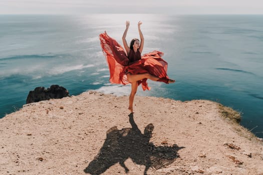 Woman red dress sea. Female dancer posing on a rocky outcrop high above the sea. Girl on the nature on blue sky background. Fashion photo