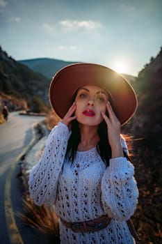 Woman road mountain. A woman in a white sweater, black boots and a hat walks along a winding alpine path between the mountains at sunset in late summer. The concept of travel