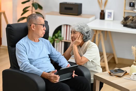 Modern senior couple enjoying talking and using digital tablet together at home.