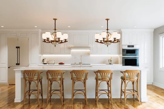 Traditional white kitchen with long island and wooden chairs with varnished wood flooring. Classic kitchen with large chandeliers and kitchen appliances. 3d rendering