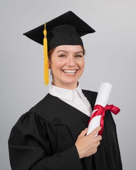 Smiling woman in graduation gown holding diploma on white background. Vertical photo