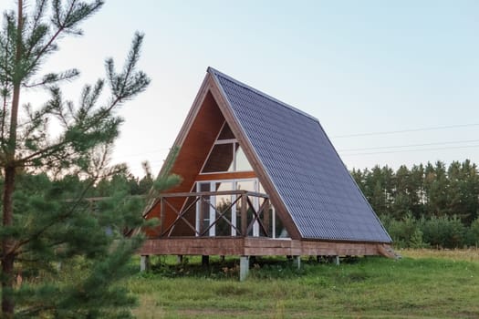 The concept of glamping and renting a chalet for weekend. Wooden house with a veranda in nature around coniferous trees.