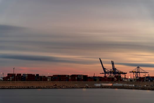 Commercial dock at twilight with containers, cranes, and smooth water surface, ideal for text placements.