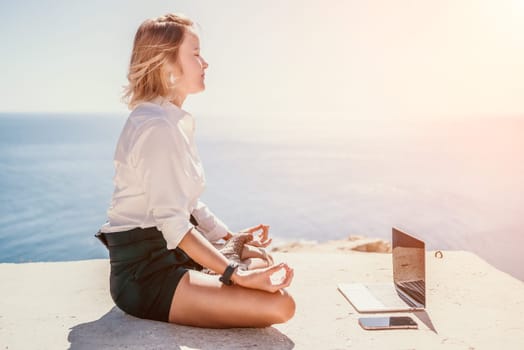 Happy girl doing yoga with laptop working at the beach. beautiful and calm business woman sitting with a laptop in a summer cafe in the lotus position meditating and relaxing. freelance girl remote work beach paradise