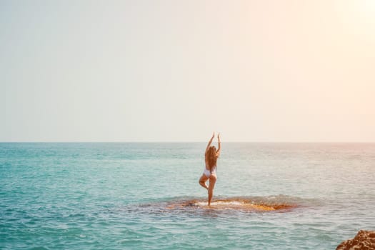 Woman sea yoga. Back view of free calm happy satisfied woman with long hair standing on top rock with yoga position against of sky by the sea. Healthy lifestyle outdoors in nature, fitness concept.