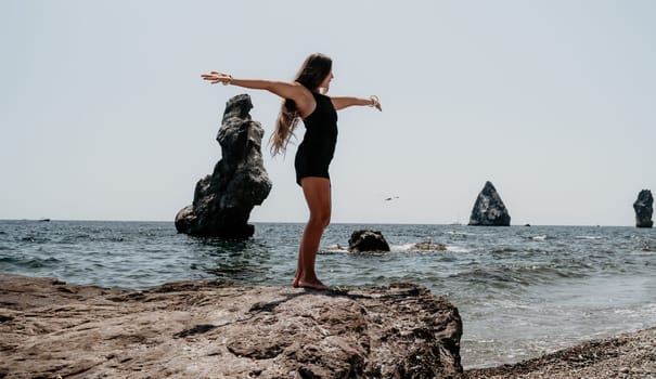 Woman travel sea. Young Happy woman in a long red dress posing on a beach near the sea on background of volcanic rocks, like in Iceland, sharing travel adventure journey