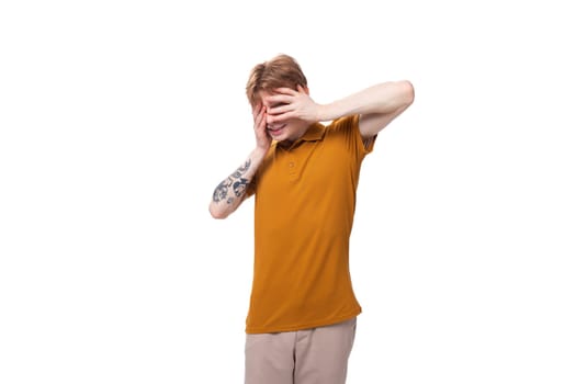 young stylish guy with red hair dressed in a mustard-colored T-shirt looks surprised.