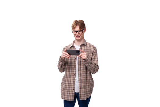 cute caucasian student guy in glasses plays a game on the phone.