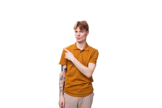 young charming red-haired man dressed in a mustard t-shirt points his hand to the side.